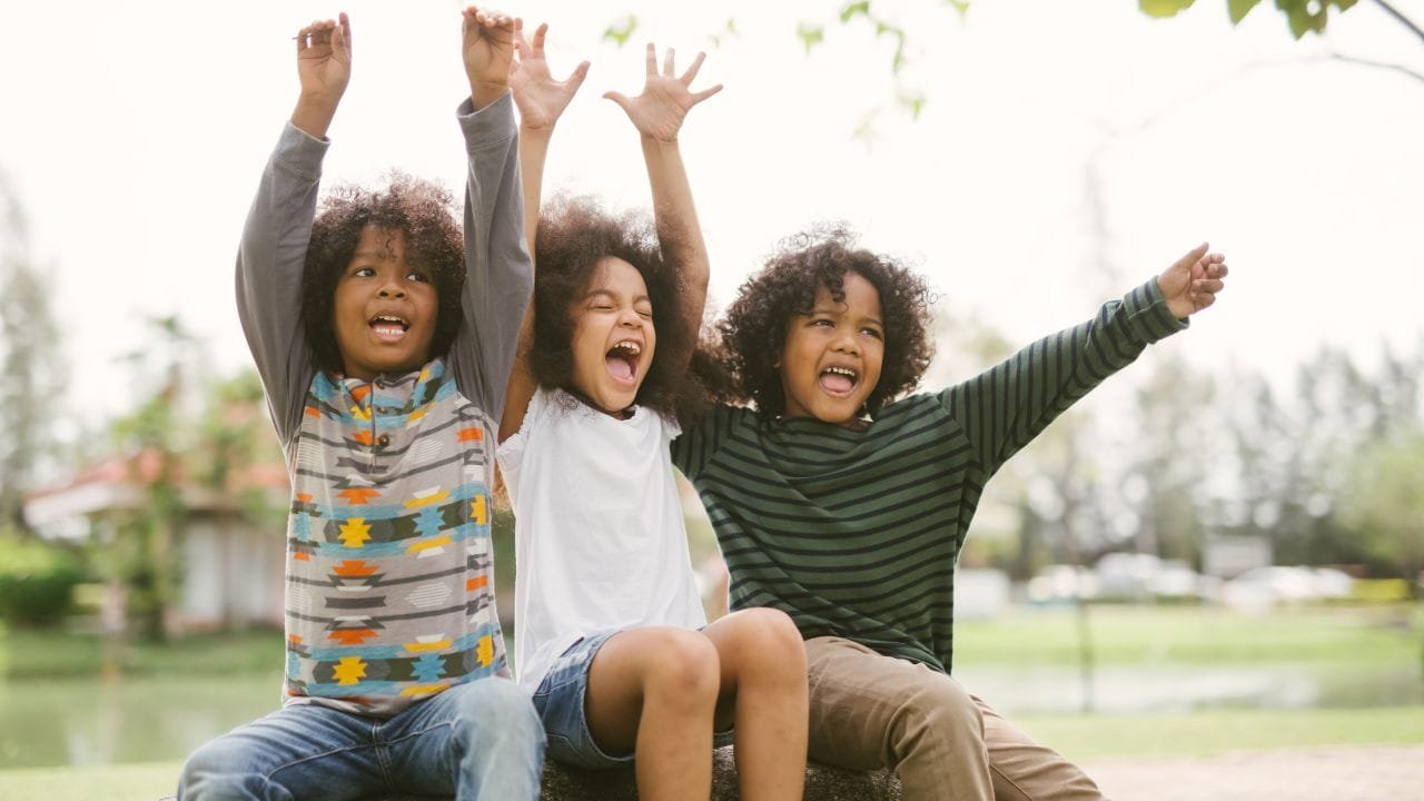 Three afro-american children sitting on a log in a park.